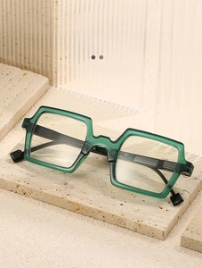 Detail view of retro green square reading glasses on a beige stone textured background