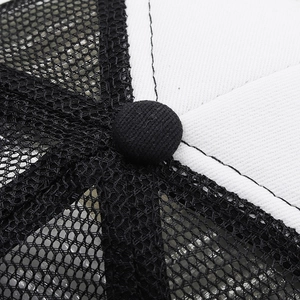 Detail view of the breathable mesh stitching and top button on a black and white trucker hat