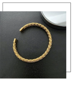 Detailed view of golden woven titanium steel open bangle on a black textured background