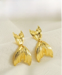 Detailed view of golden fishtail stud earrings with textured vertical ridges on fabric