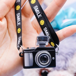 Close-up of a miniature camera keychain with a black smile lanyard in hand