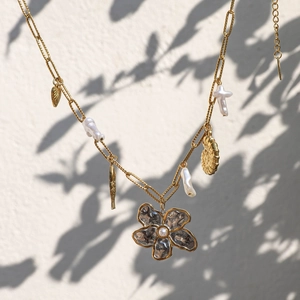 Gros plan d'un collier doré avec breloques de fleurs, de perles et de créatures marines