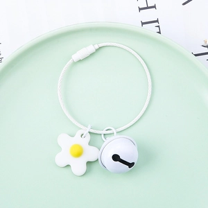 Macro shot of white silicone flower pendant and metal bell on steel wire keychain