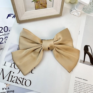 Detailed view of elegant champagne gold satin bow hair clip with smooth glossy texture