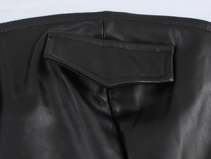 Detail of a black faux leather mini dress featuring a back flap pocket and neat stitching