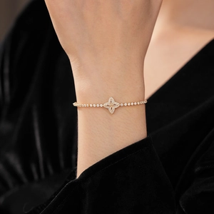 Close-up of sparkling zircon flower charm on gold adjustable bracelet worn on wrist