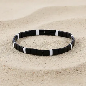 Detail of black and white Tila bead stretch bracelet displayed on golden sand background