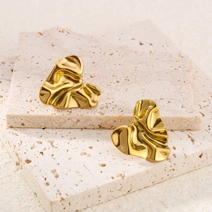 Golden irregular heart earrings with wrinkled metal texture on a stone background