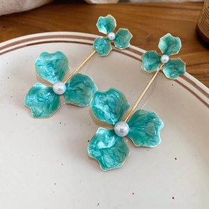 Detail of green enamel flower earrings with pearls on a vintage ceramic plate