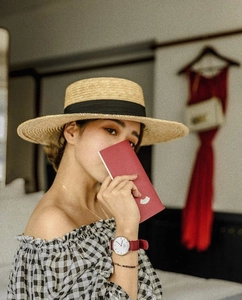 Close-up of wide-brimmed flat straw hat with black ribbon worn by a model