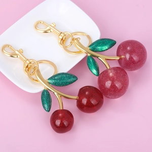 Close-up of glittery cherry keychains with gold lobster clasps and green leaves