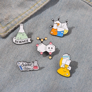 Close-up of five colorful science enamel pins with lab beaker designs on denim fabric