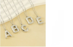 Detailed macro shot of bubble letter pendants A-E in polished silver stainless steel