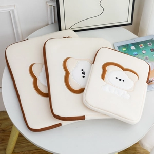 Three sizes of cream laptop sleeves featuring cartoon dog toast embroidery on a table