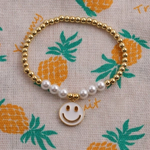 Détail d'un bracelet de perles dorées, perles blanches et pendentif smiley