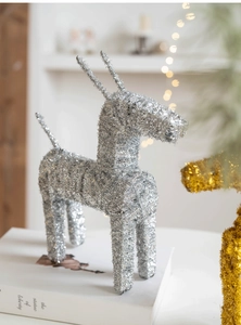 Close-up of silver sequined Christmas deer ornament on a white book with warm bokeh lights