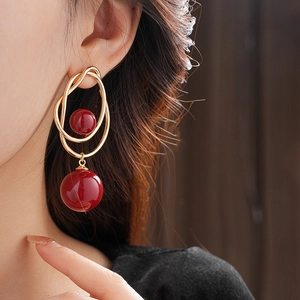 Close-up of gold double loop earrings featuring vibrant red spherical bead drops on model