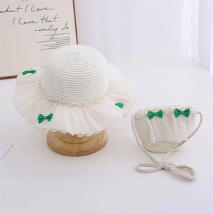 Detailed texture of straw hat with white lace trim and green satin bows for kids