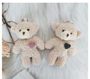 Detail of plush teddy bear keychains with knitted hearts on soft cream faux fur background