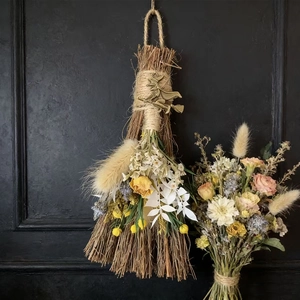 Detail of decorative holiday broom with dried flowers, twine, and metal witch charm