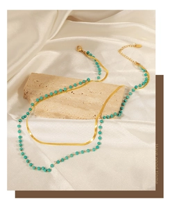 Double-layer gold snake chain necklace with turquoise beads over cream silk and stone