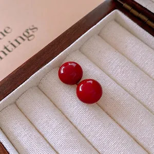 Minimalist red spherical earrings with glossy finish on cream velvet jewelry tray