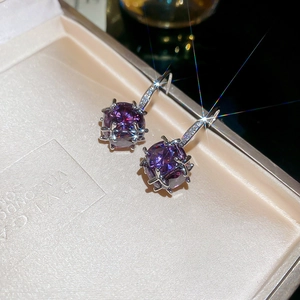 Macro shot of silver earrings featuring faceted purple stones and diamond accents
