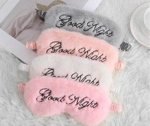 Detail view of four plush sleep masks in grey, pink, and white with Good Night embroidery