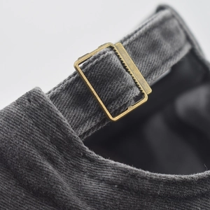 Detail of adjustable metal buckle and washed cotton fabric on the back of the grey baseball cap