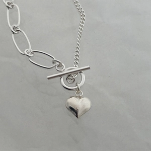 Detailed macro shot of silver heart pendant with T-bar toggle clasp on a textured surface