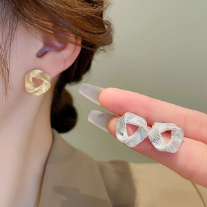 Macro shot of gold and silver twisted hoop earrings with frosted textured finish on model