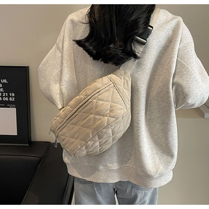 Close-up of beige quilted crossbody bag with adjustable wide strap shown on a model