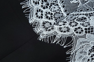 Gros plan sur la dentelle florale blanche et les franges de la robe noire moulante