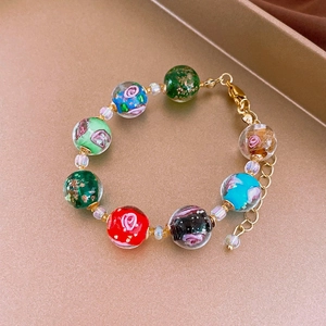 Artistic glass bead bracelet with floral patterns on a gold tray macro detail view