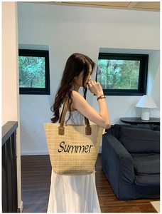 Detail view of woven straw tote bag featuring black Summer script and brown leather handles
