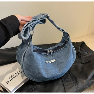 Detail view of denim crescent bag with dual zippers and adjustable strap on leather jacket