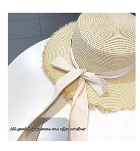 Detail of straw sun hat featuring a raw fringe edge and elegant cream ribbon bow