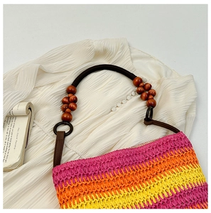 Detail of colorful rainbow straw woven bag with wooden bead handles on a white outfit