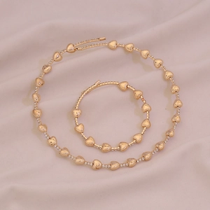 Set collana e bracciale a cuore dorato con strass su sfondo in tessuto rosa chic