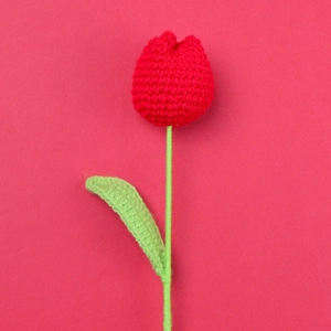 Detailed view of a handmade red crochet tulip with green stem on a red background