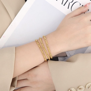 Detailed view of polished 18K gold-tone beaded stretch bracelets on a model's wrist