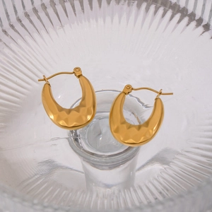 Detail of 18K gold plated U-shaped earrings with hammered texture in glass dish
