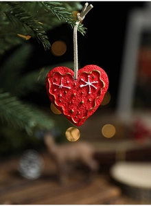 Close-up of red heart resin ornament with gold waves and snowflakes on a pine branch