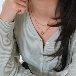 Close-up of double-layer gold heart necklace worn over mint green knitwear