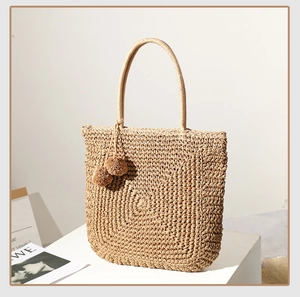Close-up of light brown straw bag with woven texture and ball tassels