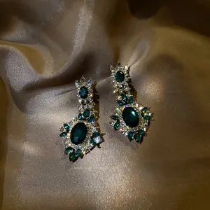 Detailed view of emerald green rhinestone drop earrings on champagne silk background