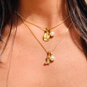 Detailed view of layered gold necklace with cowboy boot, pearl, and sunburst medal pendant
