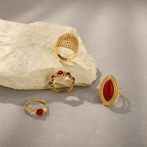Detailed close-up of four gold stainless steel rings with red gemstones on stone base
