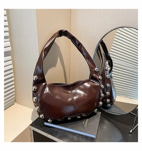 Detail of dark brown oil wax leather underarm bag with silver rivet studs and glossy finish