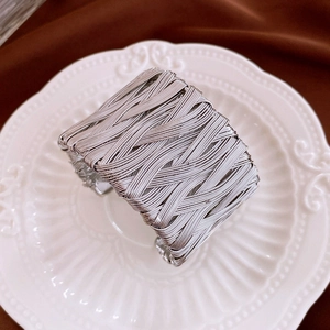 Macro shot of silver wide twisted metal bangle with woven texture on a white plate